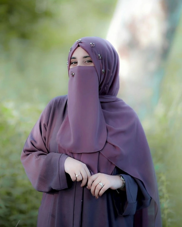A woman wearing a purple hijab standing in a field.